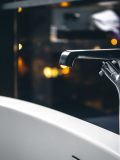 Steel faucet in the interior of a modern bathroom with a window overlooking the night city.